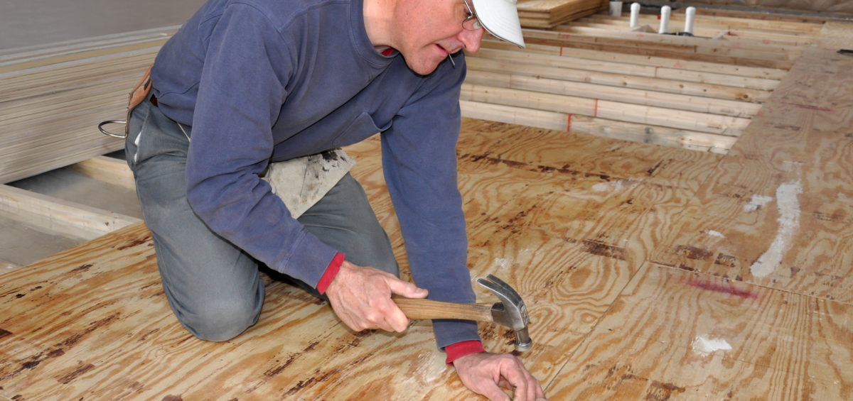 A man nailing a sub-plywood floor